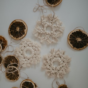 May include: Three white crocheted snowflake ornaments with gold accents and dried orange slices on a white background.