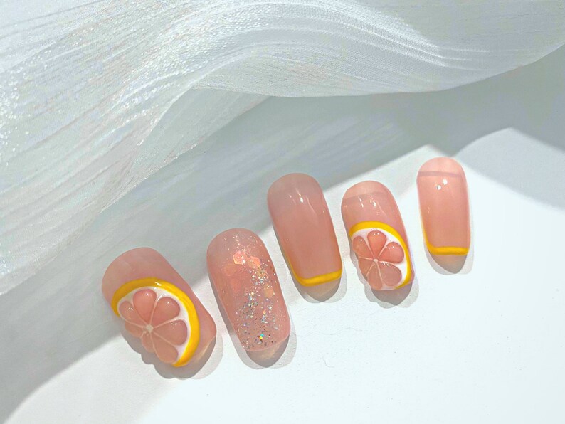 May include: Close-up of five pink and nude nails with yellow and pink lemon slice designs. Some nails have glitter.