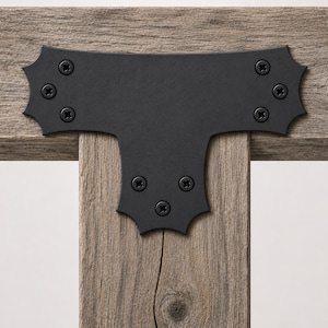 May include: A matte black metal T-shaped bracket with decorative scalloped edges, secured to weathered gray wooden beams with eight black Phillips head screws. The bracket features a wide horizontal top and a vertical base section.