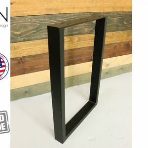 May include: Black metal table legs with a rectangular shape. The legs are made of square tubing and have a welded construction. The legs are shown against a wood background.