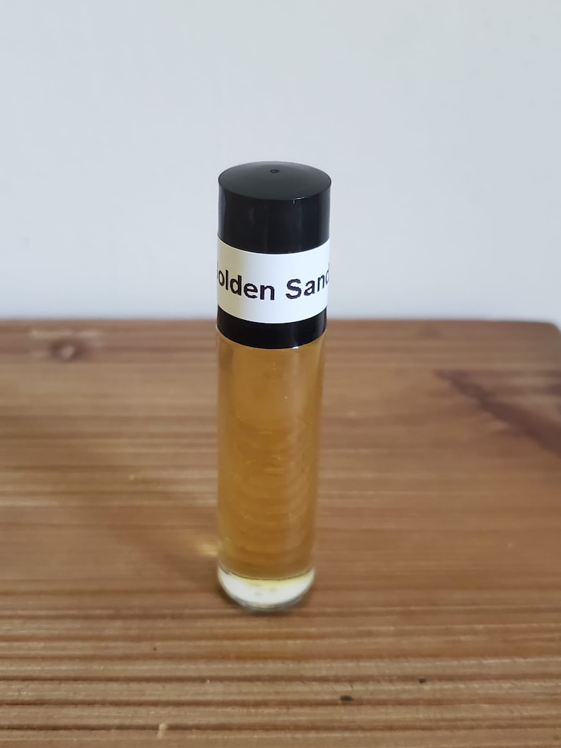 May include: A clear glass roll-on bottle with a black cap and a white label that reads "Golden Sand".