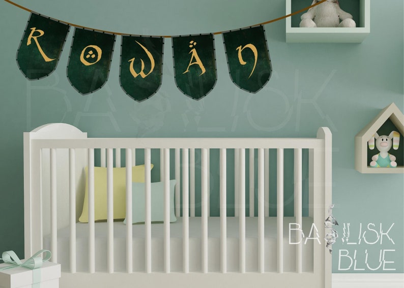 May include: A white crib with a green and gold banner that reads "ROWAN" hanging above it. The crib is in a nursery with a light blue wall and a white shelf with a stuffed animal on it.