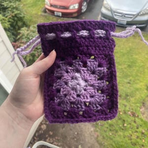 May include: A purple crocheted drawstring bag with a light purple and white square pattern in the center.