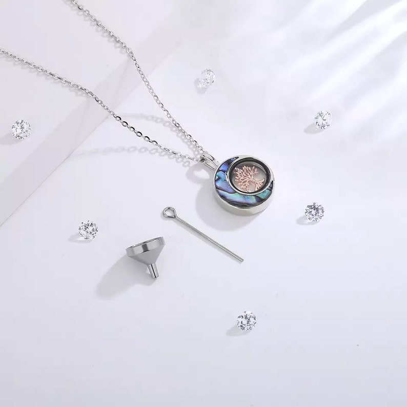 Pu&ograve; includere: Una collana d'argento con un ciondolo rotondo che presenta un design ad albero della vita. Il ciondolo &egrave; realizzato in madreperla di abalone con un design ad albero rosa. La collana viene fornita con un piccolo imbuto e uno spillo d'argento.