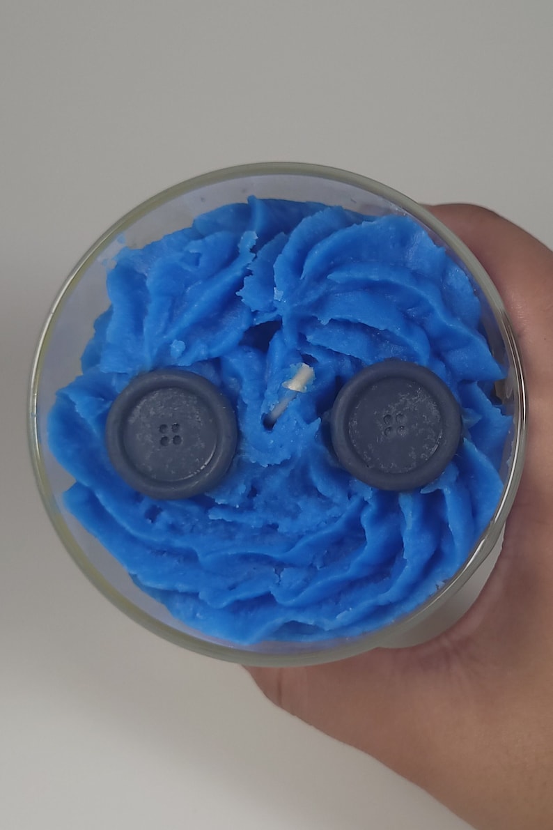 May include: A blue candle with two dark blue buttons on top. The candle is in a clear glass jar.