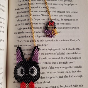 May include: A beaded necklace with two pendants. One pendant is a black bunny with a red bow tie and white eyes. The other pendant is a small beaded figure with a red head and purple body.