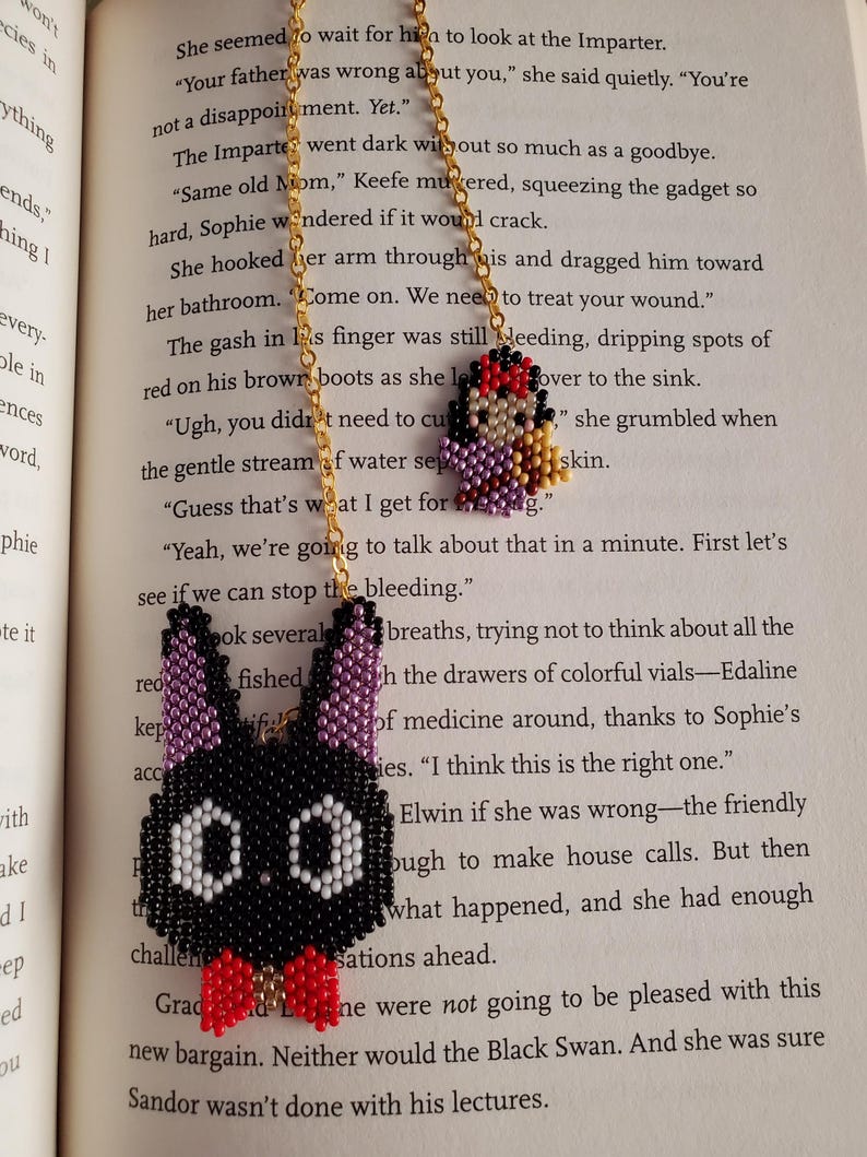 May include: A beaded necklace with two pendants. One pendant is a black bunny with a red bow tie and white eyes. The other pendant is a small beaded figure with a red head and purple body.