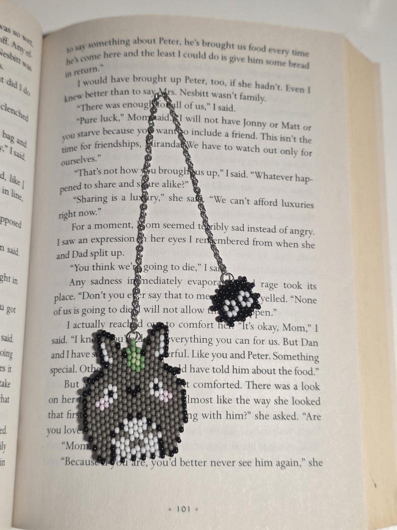 May include: A handmade beaded Totoro-inspired pendant necklace. The pendant features a gray Totoro design with white, black, and pink accents, and a small green leaf. The necklace has a silver chain and a small black beaded charm.