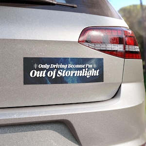 May include: A silver car with a bumper sticker that reads "Only Driving Because I'm Out of Stormlight". The sticker has a blue and black background with a lightning bolt and a compass.