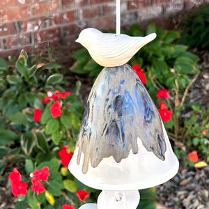 May include: A ceramic wind chime with a white bird on top and a bell shaped like a mushroom with a blue and brown glaze.