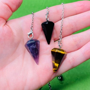 May include: Three crystal pendulums on silver chains. The pendulums are black, purple, and brown with gold streaks.