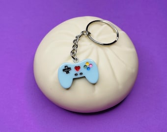 May include: A light blue video game controller keychain with a red heart and colorful buttons attached to a silver key ring.
