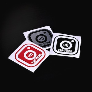 May include: Three stickers with a camera icon and the text "Tap Here" in white. The stickers are on a black background. The stickers are red, black, and gray.