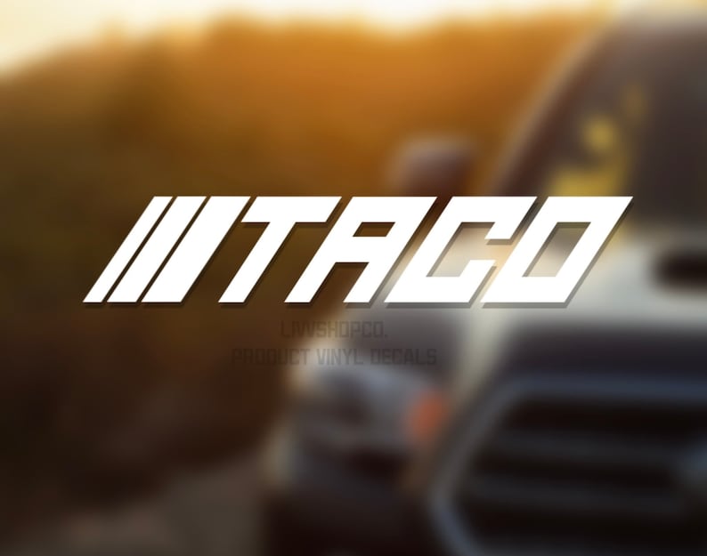 Peut inclure: Autocollant en vinyle blanc avec le mot "TACO" dans une police de caract&egrave;res audacieuse et stylis&eacute;e. L'autocollant est plac&eacute; &agrave; l'arri&egrave;re d'un camion argent&eacute;.