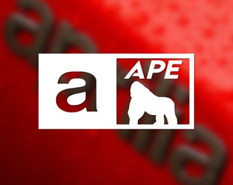Może przedstawiać: Biała naklejka z napisem "APE" wielkimi literami i sylwetką goryla. Naklejka zawiera również literę "a" w większej czcionce.