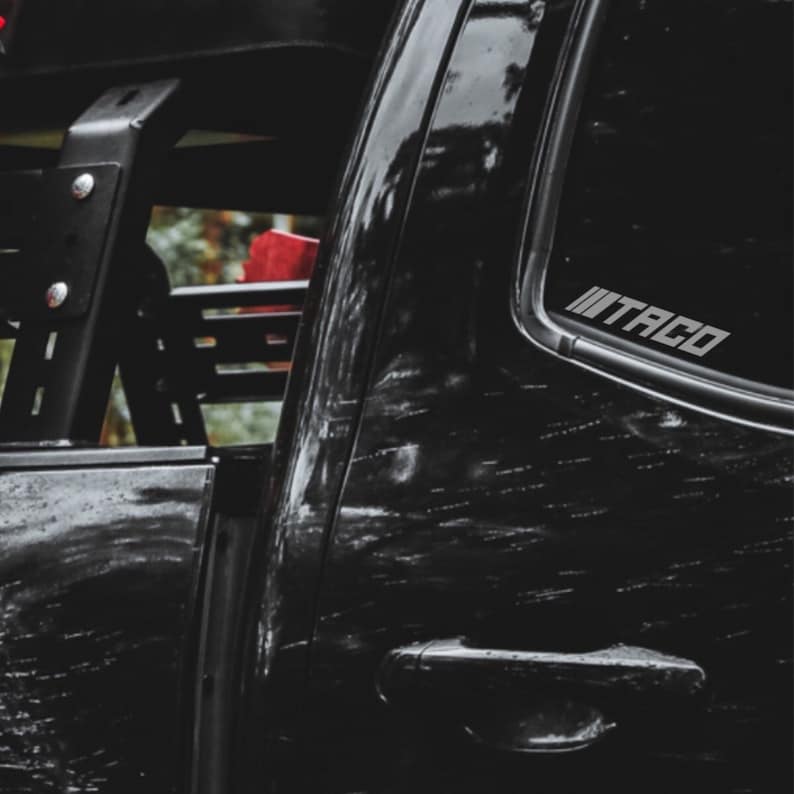 Peut inclure: Un camion pick-up noir avec un arceau de s&eacute;curit&eacute; noir et un autocollant "TACO" sur la vitre arri&egrave;re.