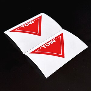 May include: Two white stickers with red triangle shapes and the word "TOW" printed in white letters.