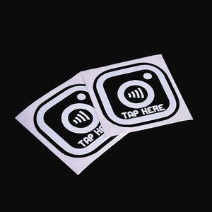 May include: Two white square stickers with black Instagram icons and the text "Tap Here" printed on them.