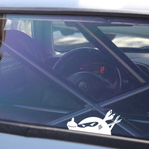 May include: A white sticker of a cartoon character with a middle finger on a car window. The character is wearing a helmet and has a sword in its hand.