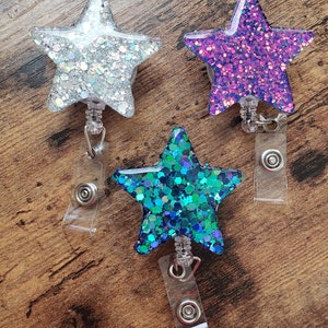 May include: Three sparkly star-shaped badge holders with clear retractable reels. The stars are silver, purple, and teal.