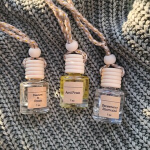 May include: Three small glass bottles with wooden tops and hanging cords. Each bottle has a label with a different scent: Peaches & Cream, April Fresh, and Strawberry Shortcake. The bottles are 7 ml each.