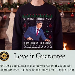 May include: A black long-sleeve sweatshirt featuring a graphic of a character in a blue suit and red tie. The text reads "ALMOST CHRISTMAS" and "MEANS IT WASN'T CHRISTMAS!" surrounded by green and red holiday patterns including reindeer and ornaments.