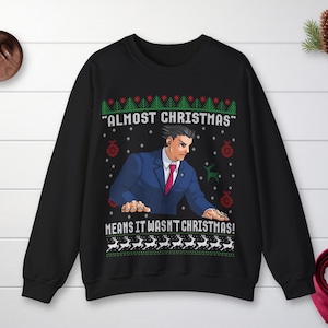 May include: A black crewneck sweatshirt featuring a graphic of a character in a blue suit and red tie. The text reads "ALMOST CHRISTMAS" and "MEANS IT WASN'T CHRISTMAS!" surrounded by green pine trees, red ornaments, and white reindeer patterns.