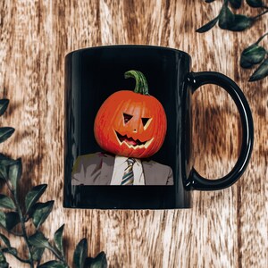 May include: Black coffee mug with a white-collar worker wearing a pumpkin for a head. The pumpkin has a carved jack-o'-lantern face.