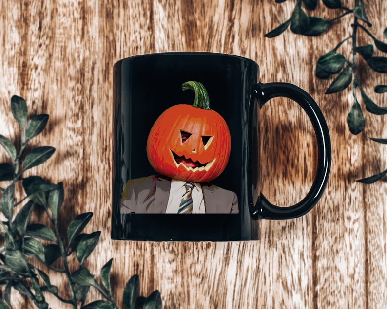 May include: Black coffee mug with a white-collar worker wearing a pumpkin for a head. The pumpkin has a carved jack-o'-lantern face.