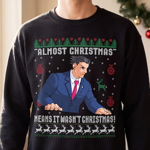 May include: A black crewneck sweatshirt featuring a graphic of a character in a blue suit and pink tie. The text reads "ALMOST CHRISTMAS" and "MEANS IT WASN'T CHRISTMAS!" surrounded by green pine trees, red ornaments, and white reindeer patterns.