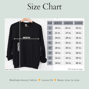 May include: A black crew neck sweatshirt on a wooden hanger with a size chart displaying width, length, and sleeve measurements in inches for sizes S through 5X. The chart includes the text Gildan 18000 Crew Neck, Medium-heavy fabric, Loose fit, and Runs true to size.