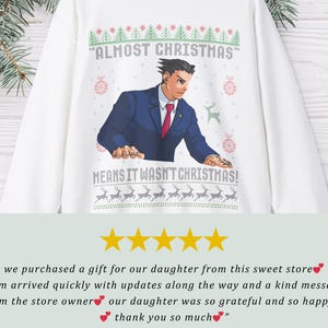 May include: A white long-sleeve sweatshirt featuring a graphic of a character in a blue suit and red tie. The text reads ALMOST CHRISTMAS MEANS IT WASN'T CHRISTMAS, surrounded by green and red holiday patterns including reindeer and ornaments.