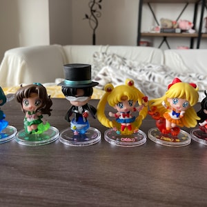 Puede incluir: Colecci&oacute;n de seis figuras de estilo anime. Cada figura est&aacute; sobre una base transparente y circular. Las figuras presentan colores vibrantes, incluyendo azul, verde, amarillo, naranja y rojo. Los personajes tienen ojos grandes y trajes detallados.