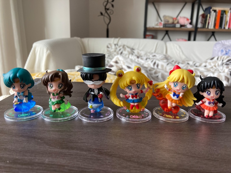Puede incluir: Colecci&oacute;n de seis figuras de estilo anime. Cada figura est&aacute; sobre una base transparente y circular. Las figuras presentan colores vibrantes, incluyendo azul, verde, amarillo, naranja y rojo. Los personajes tienen ojos grandes y trajes detallados.