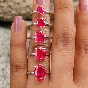 May include: A set of five silver rings with oval-shaped red gemstones. The rings are arranged in order of size, with the smallest ring on the left and the largest ring on the right.