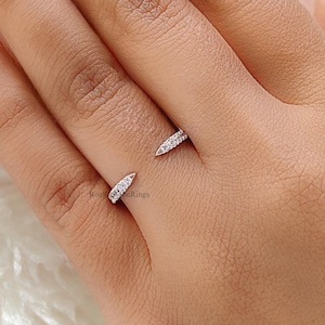 May include: A silver ring with a pointed design and small clear stones. The ring is worn on a finger with light pink nail polish.