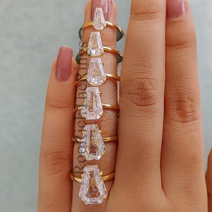 Może przedstawiać: Zestaw siedmiu złotych pierścionków z różnymi rozmiarami przezroczystych, fasetowanych, łzowych kamieni.