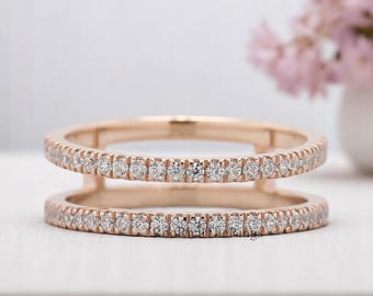 May include: A rose gold double-band ring with a continuous row of small, clear gemstones. The ring has a modern design with two parallel bands connected by small vertical supports. The gemstones sparkle against the warm metal.
