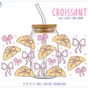 Puede incluir: Un envoltorio de lata de vidrio transparente con tapa de madera y pajita de vidrio. El envoltorio presenta un patrón repetido de cruasanes amarillos con lazos rosas. El texto "CROISSANT 16oz GLASS CAN WRAP" se muestra en rosa.