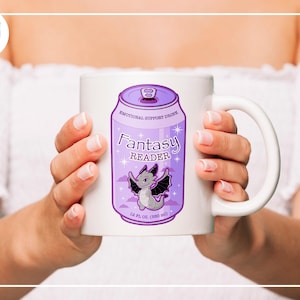 May include: White ceramic mug featuring a purple can design with the words "Fantasy Reader" and a cartoon dragon illustration. The mug also includes the text "Emotional Support Drink" and "18 fl oz (530 ml)".