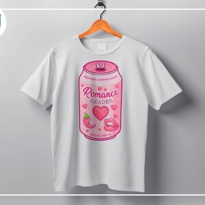 May include: White t-shirt featuring a pink soda can design. The can reads "Romance Reader" with hearts, a chili pepper, and lips. The can is labeled "Emotional Support Drink" and has a volume of 12 fl oz (360 ml).