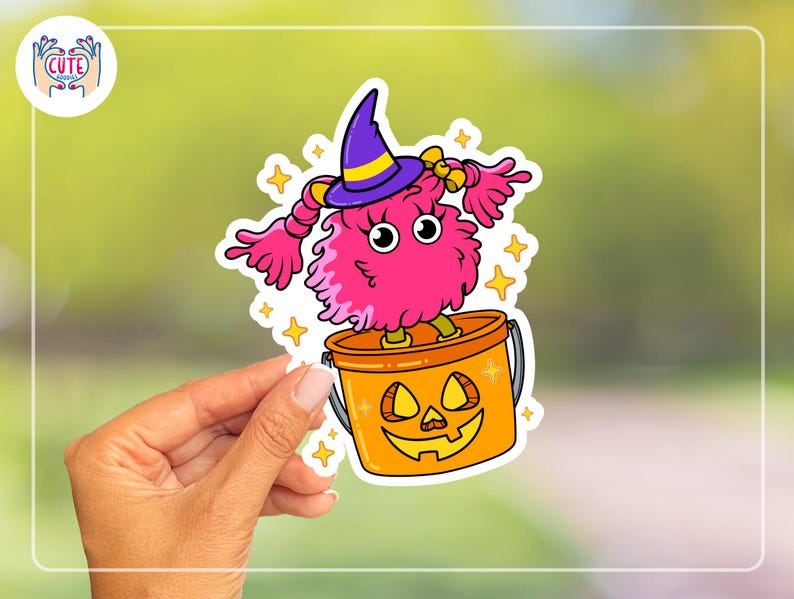 K&ouml;nnte beinhalten: Ein farbenfroher Halloween-Aufkleber mit einem rosa, flauschigen Monster, das einen lila Hexenhut mit gelbem Band tr&auml;gt. Das Monster steht in einem orangefarbenen K&uuml;rbis-Eimer. Gelbe Sterne umgeben das Monster und den Eimer.