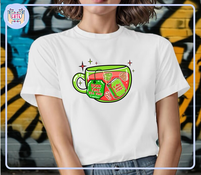 May include: White t-shirt featuring a whimsical illustration of a teacup filled with festive elements. The teacup design includes a tag that reads "Book Time Tea Time" and a book with the text "X-Mas Warm Stories".