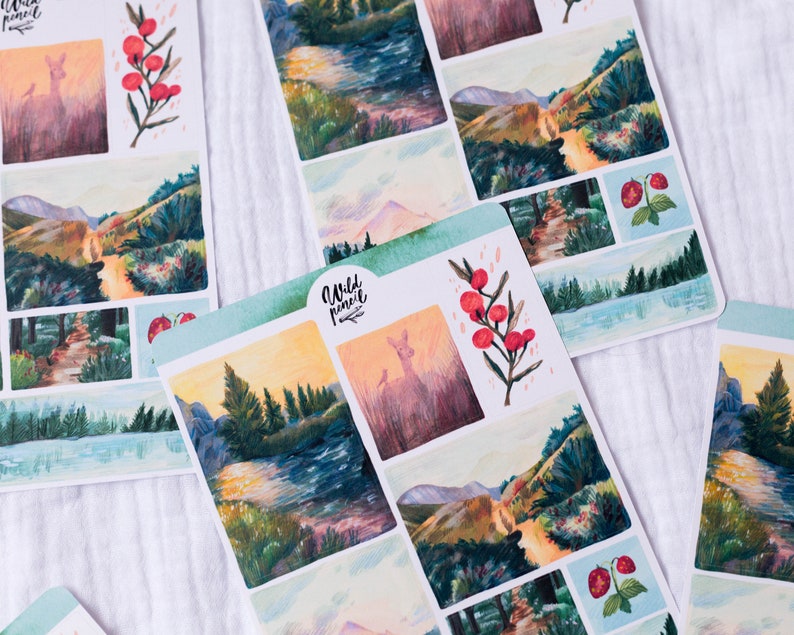 May include: A sheet of stickers featuring watercolor illustrations of nature scenes. The stickers include a deer, a mountain path, a river, and a forest. The stickers are printed on white paper with a light blue border.