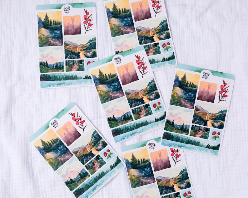 May include: A set of six watercolor stickers featuring a mountain landscape with a river, trees, and a deer. The stickers are printed on white paper and have a glossy finish. The stickers are perfect for adding a touch of nature to your planner, journal, or scrapbook.