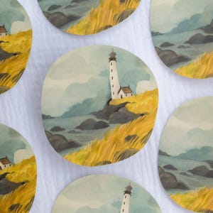 Op de afbeelding: Set van zes aquarellen met een vuurtoren op een rotsachtige kust met geel gras. De schilderijen zijn rond en hebben een witte achtergrond.