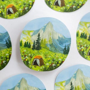 Op de afbeelding: Een set van zes geïllustreerde stickers met een bergketen met een tent in een veld vol wilde bloemen. De stickers zijn rond en hebben een witte achtergrond.
