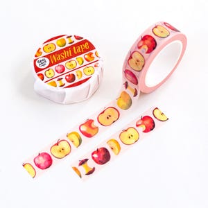 Puede incluir: Un rollo de cinta washi de color rosa claro con un patrón repetitivo de acuarelas de manzanas rojas, amarillas y verdes y corazones de manzana. La etiqueta del envase muestra el texto Washi tape en amarillo sobre fondo rojo.
