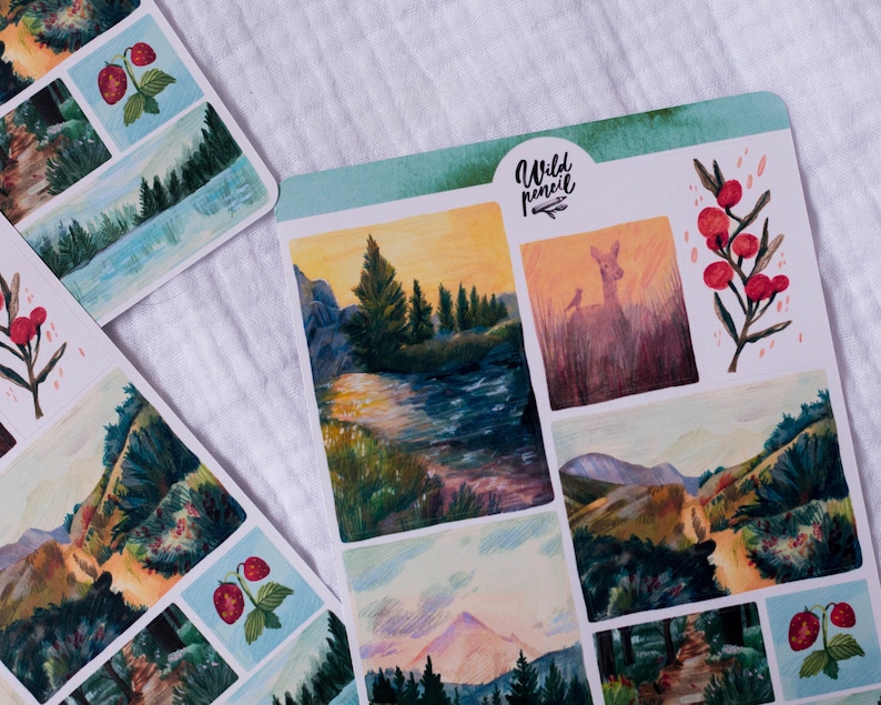 May include: A sheet of stickers with a watercolor aesthetic featuring nature scenes. The stickers include a deer in a field, a mountain range, a forest path, a river, and a berry branch. The stickers are labeled "Wild Pencil".