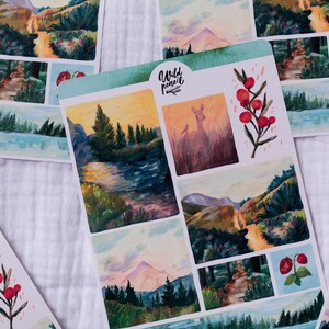 May include: A sheet of stickers featuring watercolor illustrations of nature scenes. The stickers include a deer in a forest, a mountain range, a river, and a path through a forest. The stickers are printed on white paper with a light blue border.